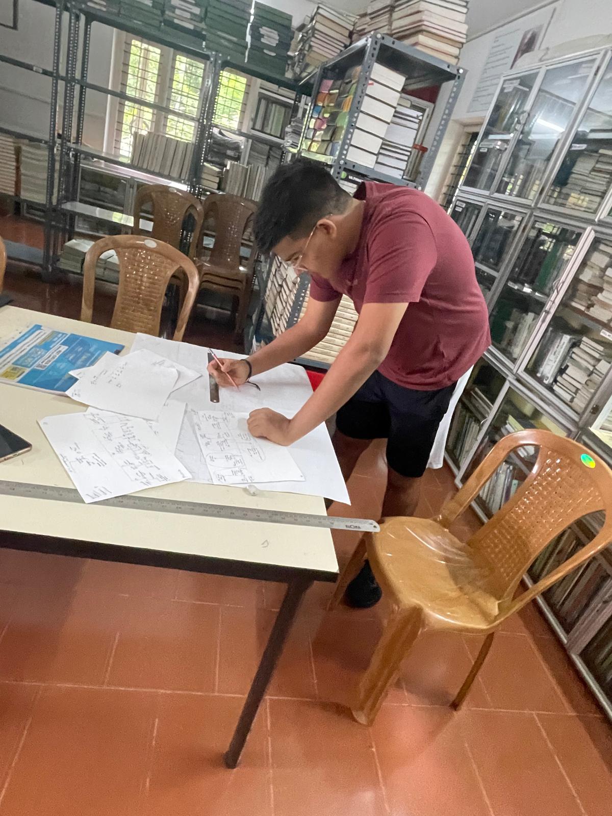Aveer drawing a hand-written kinship chart on large sheets of paper in a research library