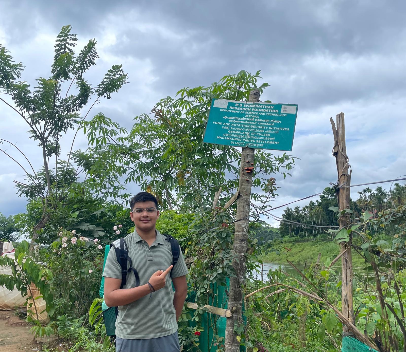 Aveer beside an M. S. Swaminathan Research Foundation sign at the Madamkunnu Paniya settlement